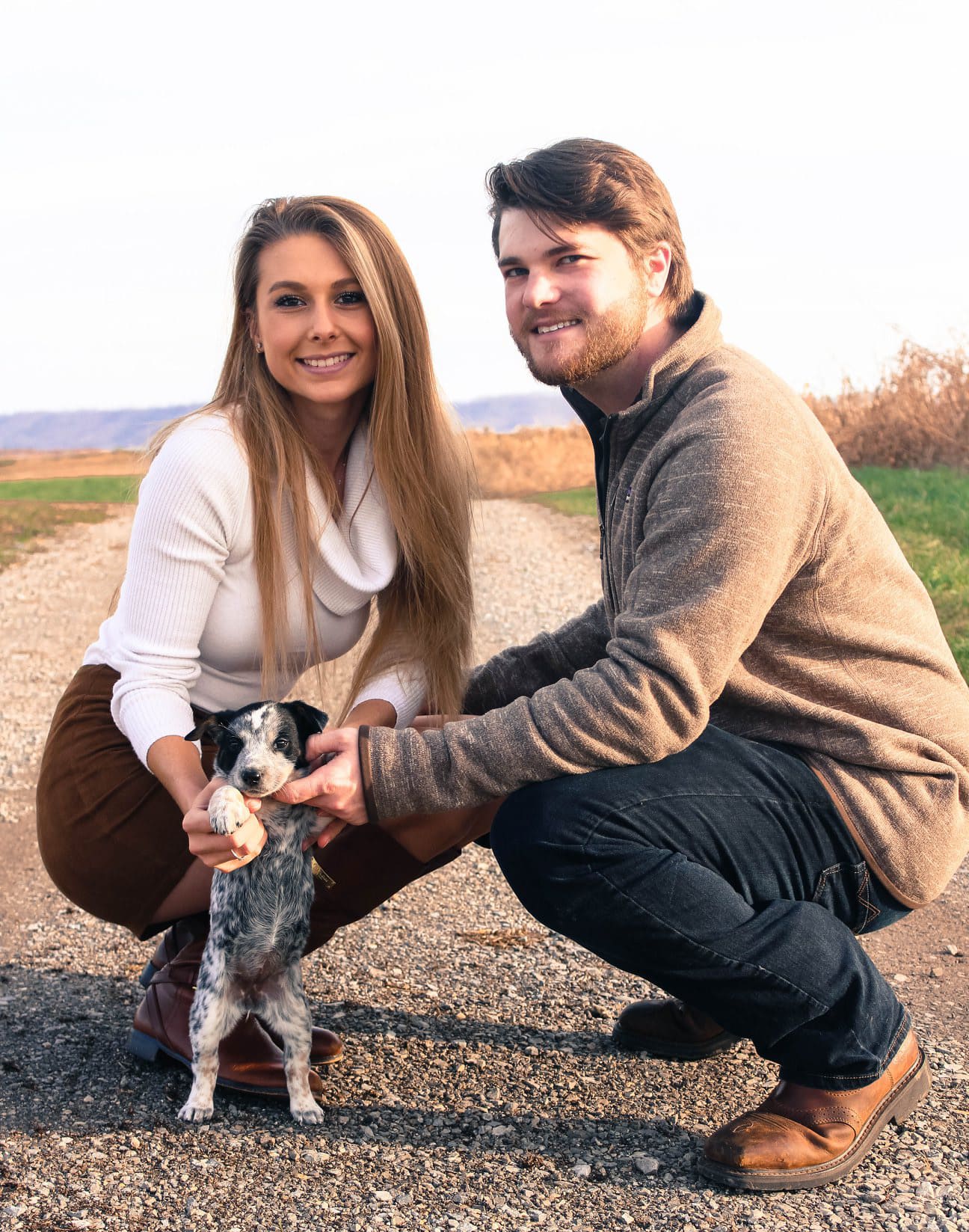 Couple kneeling in a field with their puppy